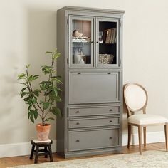 a tall cabinet with glass doors next to a chair and potted plant on the floor