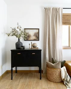 a living room with white walls and wooden floors, a black table with two vases on it next to a brown leather couch