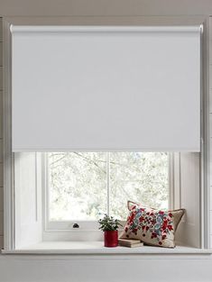 a window with white roller shades and pillows