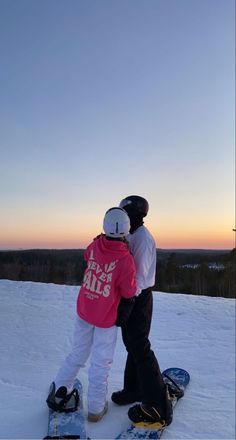 two snowboarders embracing each other on the top of a hill at sunset or dawn