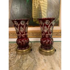 two red vases sitting next to each other on a marble counter top in front of a painting