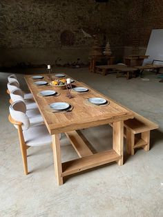 a wooden table with white chairs and plates on it in an empty room next to a brick wall