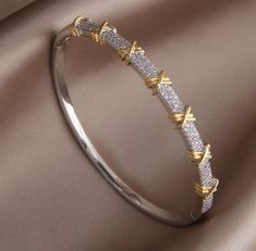 Elevate your style with our stunning Two-Tone Crystal Bangle Bracelet, an exquisite piece of jewelry that perfectly blends elegance and sophistication. This bracelet features a unique design with alternating bands of silver and gold, adorned with sparkling crystal accents that catch the light beautifully. The distinctive gold X details add a touch of modern charm, making this bangle a versatile accessory for any occasion. Crafted with high-quality materials, this bangle bracelet is both durable Unique Bracelets Gold, Modern Gold Jewelry Unique Designs, Modern Bangle, Necklace Chain Types, Modern Gold Jewelry, Jewelry Illustration, The Bangles, Bracelets Design, Crystal Bangle