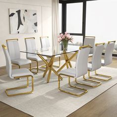 a dining room table with white chairs and a vase on the floor in front of a large window