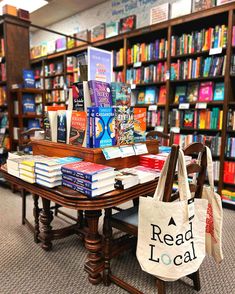 there are many books on the table in the library and one bag is sitting next to it