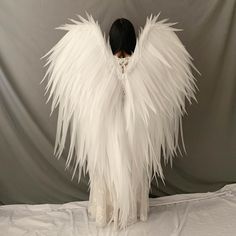 a woman with white feathers on her body standing in front of a gray backdrop and wearing an angel costume