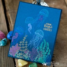 a blue card with jellyfish on it sitting next to some rocks and seaweed