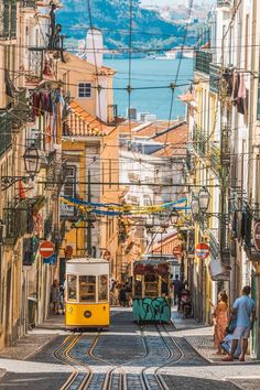 two people are standing on the street next to a yellow trolley car in an alleyway