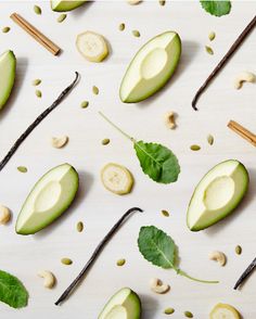 an avocado cut in half with leaves and nuts scattered around it on a white surface