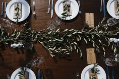 the table is set with white plates and silverware, greenery, and napkins