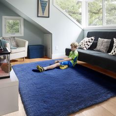 a young boy sitting on the floor in front of a blue area rug with pillows