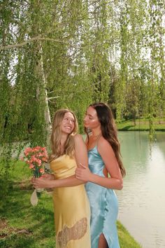 two beautiful young women standing next to each other in front of a lake and trees