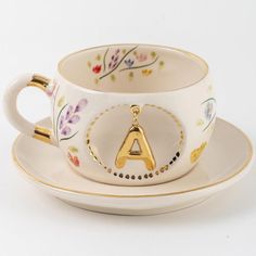 a tea cup and saucer with the letter a on it, decorated with flowers