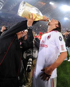 a man drinking from a bottle while standing next to another man on a soccer field