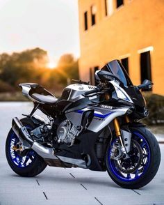 a silver and blue motorcycle parked in front of a building with the sun behind it