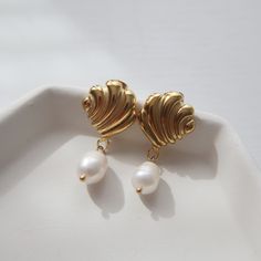 Adorned with a seashell and pearl dangle, these earrings are perfect for adding a beachy and fun flair to any look. -stainless steel, gold plated Pearl Shell Drop Earrings With Pearl Drop Detail, Gold Shell With Pearl Drop, Gold Pearl Shell-shaped Earrings, Elegant Shell-shaped Earrings, Elegant Shell-shaped Metal Earrings, Gold Shell Earrings With Pearl Charm, Gold Dangle Shell Earrings With Pearl Drop, Gold Pearl Charm Earrings For Beach, Gold Shell-shaped Pearl Earrings