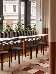 an empty restaurant with striped seats and tables in front of large windows overlooking the city