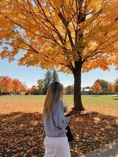 a woman standing under a tree with leaves on the ground