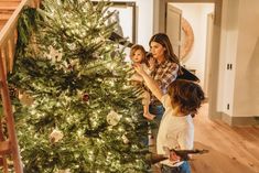 two children and an adult are decorating a christmas tree