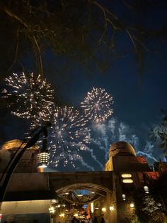 fireworks in the night sky over a building with people walking on it and some trees