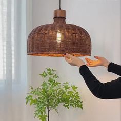 a woman reaching for something under a light fixture in her living room with a potted plant on the table