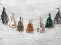 an assortment of leaf ornaments hanging from a string on a white brick wall in the shape of christmas trees