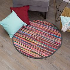 a round rug with colorful stripes on the floor next to a chair and pillows in a living room