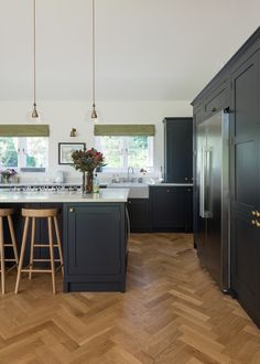 a large kitchen with wooden floors and black cabinets, two stools in front of the island