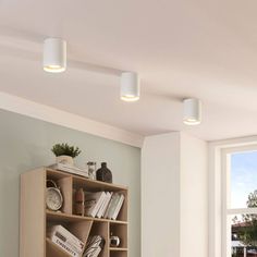 three lights that are on the ceiling above a book shelf in a room with white walls