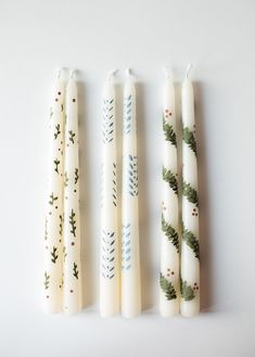 three candles are lined up next to each other on a white surface with pine branches painted on them