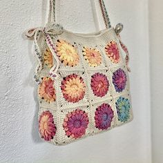 a crocheted bag hanging from a hook on a wall with flowers in it