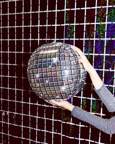 a woman holding up a disco ball in front of a wall with squares on it