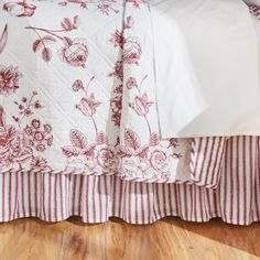 a bed with red and white bedspread on top of wooden floor next to wall