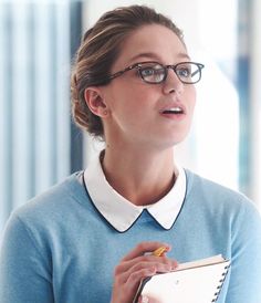 a woman wearing glasses holding a notebook and pen