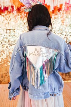 the back of a woman wearing a jean jacket with fringes and just married on it