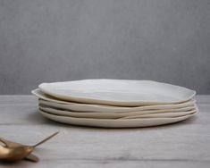 four white plates stacked on top of each other next to a gold fork and spoon