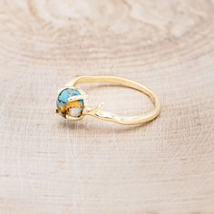 a gold ring with a blue and yellow stone in it sitting on a wooden surface