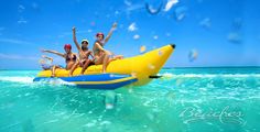 four people are riding on an inflatable banana boat through the blue ocean water