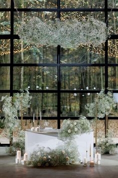 a table with flowers and candles on it in front of a window that has lights hanging from the ceiling