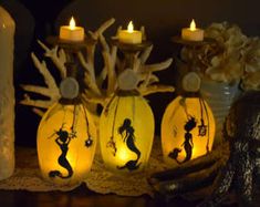 three lit up vases sitting on top of a table next to candles and flowers