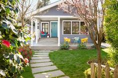 a blue house with white trim and green grass in the front yard is surrounded by trees