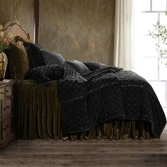 a bed with black and gold comforters in a room next to a window,