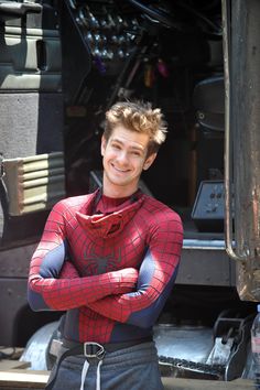 a young man dressed as spider - man standing in front of a truck with his arms crossed