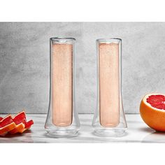 two tall vases filled with liquid next to grapefruit and blood orange slices