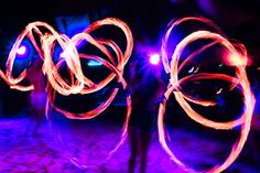 two people standing in the dark with long exposures on their hands and holding fire sticks