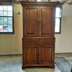 a large wooden cabinet sitting in the middle of an unfinished room with two windows behind it