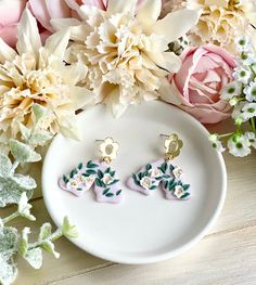 two flower shaped earrings sitting on top of a white plate next to pink and white flowers