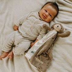 a baby laying on top of a bed next to a teddy bear bag with a stuffed animal in it