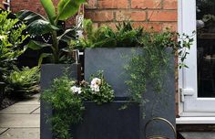 two planters with plants in them sitting on the ground next to a brick building