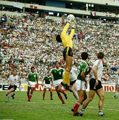 a soccer player jumps up to head the ball as other players watch from the sidelines